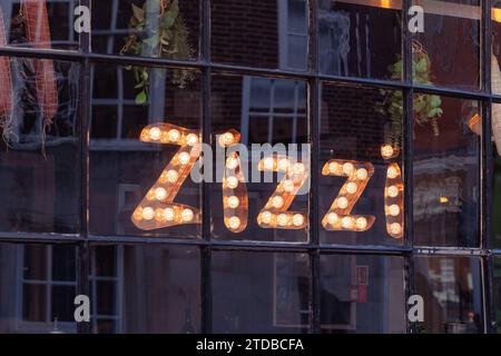 Beleuchtetes Schild aus Glühbirnen im vorderen Fenster eines Zizzi Restaurants an der Winchester High Street, Großbritannien. Die Azzurri-Gruppe betreibt Zizzi Stockfoto