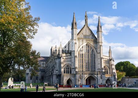 Die Westfassade (oder Westfront) der gotischen Winchester Cathedral in der späten Nachmittagssonne mit einem Mohnbanner und Besuchern. UK Stockfoto