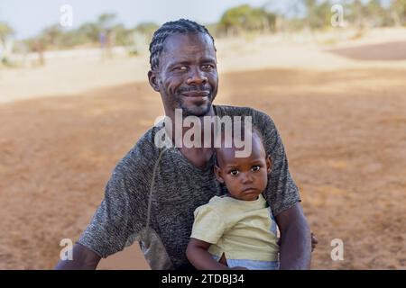 Dorf junger afrikanischer Vater mit Kind, stehend im Hof an einem sonnigen Tag, Mann mit Dreadlocks Frisur Stockfoto
