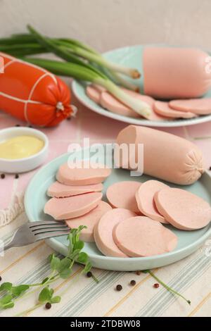 Zusammensetzung mit gekochter Wurst auf dem Teller, grünen Zwiebeln und Sauce auf einem rosa Fliesentisch Stockfoto