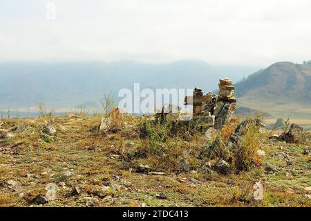 Rituelle Steinpyramiden auf einem Hügel mit Blick auf ein wunderschönes Tal, umgeben von Bergen mit Nebel auf den Gipfeln. Altai, Sibirien, Russland. Stockfoto