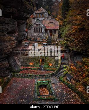 Hresko, Tschechische Republik - Blick aus der Vogelperspektive auf ein schönes Steinhaus in den tschechischen Wäldern in der Nähe von Hresko im Herbst mit farbenfrohem Herbstlaub und Mann in rotem Jack Stockfoto