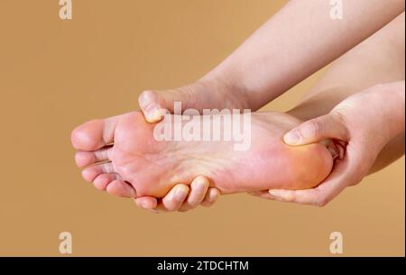 Eine Frau mit starken Plantarschmerzen massiert ihren Fuß, isoliert auf beigefarbenem Hintergrund Stockfoto