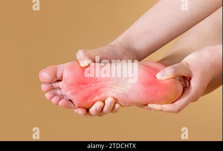 Frau mit starken plantaren Schmerzen massiert ihren Fuß, isoliert auf beigefarbenem Hintergrund (rot markiert) Stockfoto