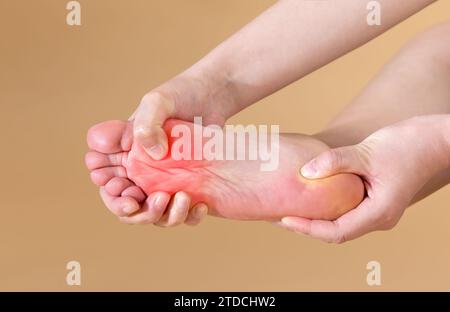 Frau mit starken plantaren Schmerzen massiert ihren Fuß, isoliert auf beigefarbenem Hintergrund (rot markiert) Stockfoto