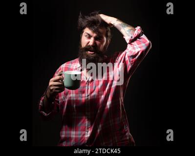 Mans hält eine Tasse Kaffee und Gähnen. Morgentee. Gähngesicht. Mann mit Teetasse. Hipster-Mann gähnt mit einer Tasse Kaffee. Bärtiger Mann, der gähnt, hält mu Stockfoto