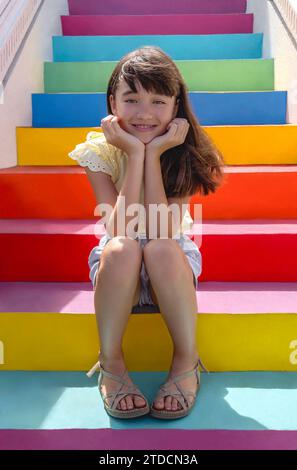 Elfjähriges Mädchen, das auf bunten Treppen sitzt Stockfoto