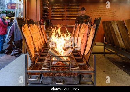 Bonn - 16. Dezember 2023 : Blick auf geflammten Lachs über Buchenholz auf dem Bonner Weihnachtsmarkt Stockfoto