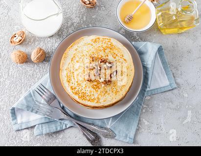 Blick von oben auf einen großen Stapel Crepes mit Honig und Walnüssen, Honig in einem Glas, Milch in einem Krug. Traditionelles Frühstück für einen Frühlingsurlaub in Russland Stockfoto