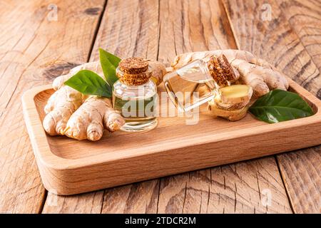 Zwei Glasflaschen mit Korkdeckel mit natürlichem Bio-Ingwerwurzelöl auf einem Holztablett zwischen Ingwerwurzeln. Tonic-Produkt Stockfoto