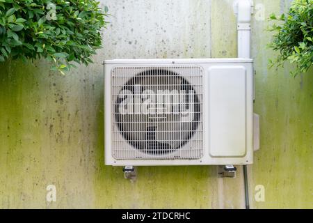 Die Außeneinheit des Klimaanlagenkompressors wird an einer verschmutzten Betonwand außerhalb des Hauses oder Büros installiert. Stockfoto