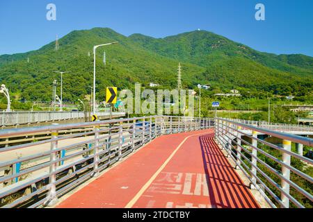 Hanam City, Südkorea - 1. Oktober 2023: Von der Paldang Bridge aus erstreckt sich ein ruhiger Fahrradauslauf, der die grüne Kulisse des Yebongsan Mountains umrahmt. Stockfoto