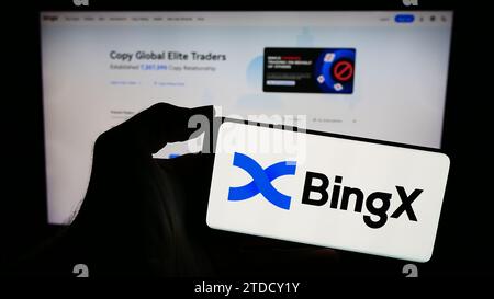 Person, die ein Mobiltelefon mit dem Logo der Kryptowährungsbörse BingX vor der Business-Website hält. Schwerpunkt auf dem Display des Telefons. Stockfoto