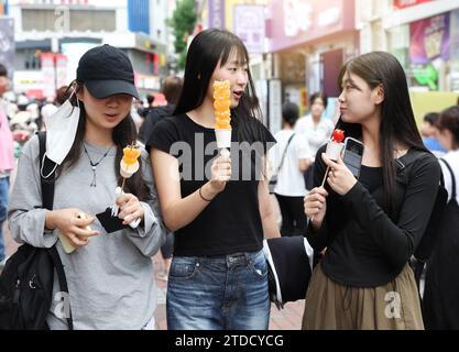 Studentinnen gehen zu Fuß, während sie Tanghulu, einen traditionellen chinesischen Snack, auf einer Straße in Korea essen Stockfoto