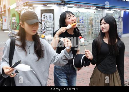 Studentinnen gehen zu Fuß, während sie Tanghulu, einen traditionellen chinesischen Snack, auf einer Straße in Korea essen Stockfoto