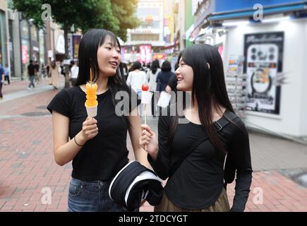 Studentinnen gehen zu Fuß, während sie Tanghulu, einen traditionellen chinesischen Snack, auf einer Straße in Korea essen Stockfoto