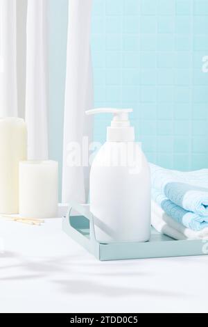 Gefaltete Handtücher und eine Flasche weißes Duschgel befinden sich auf einem Tablett. Weißer Tisch mit Kerzen. Eleganter Raum mit zwei Hauptfarben: Stockfoto