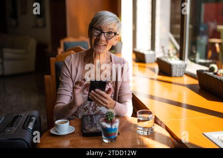 Reife Frau sitzt in einem Café am Flughafen und wartet auf das Boarding. Stockfoto