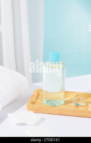 Eine transparente Flasche Make-up-Entferner und ein Glasmarmor befinden sich auf einem Holztablett. Ein Handtuch und Wattepads auf einem weißen Tisch. Kopierbereich. Stockfoto