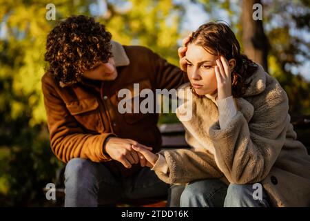 Das junge Paar sitzt am sonnigen Tag im Park. Die Frau ist traurig und ein Mann, der sie tröstet. Stockfoto