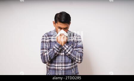 Junger erwachsener asiatischer Mann bedeckt Nase und Mund mit Gewebe, wenn er auf weißem Hintergrund niest. studio-Aufnahme Stockfoto