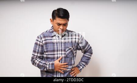Junger asiatischer Mann mit schmerzhaften Magenschmerzen auf weißem Hintergrund Stockfoto