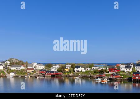 Reine, die mit klassischen roten Rorbu-Häusern auf einer schmalen Landzunge in der ruhigen blauen Nordsee geschmückt ist, sonnt sich an einem ruhigen, sonnigen Sommertag in der Ruhe Stockfoto