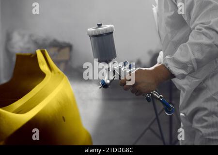 Professioneller männlicher Autolackierer sprüht Autoteile in der Garage mit dem Airbrush auf Goldfarbe. Der Mann arbeitet mit der Spritzpistole. Stockfoto