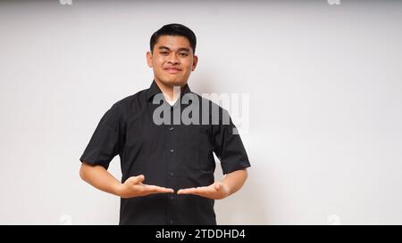 Junger asiatischer Mann lächelt mit einer Hand, die etwas auf weißem Hintergrund hält Stockfoto