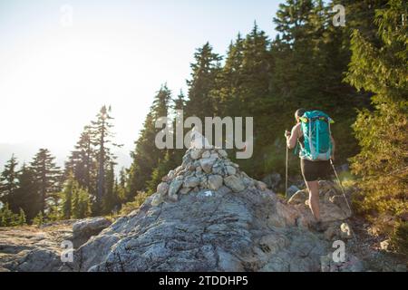 Rückansicht des Backpackers beim Wandern neben dem großen Steinhaufen auf dem Trail. Stockfoto