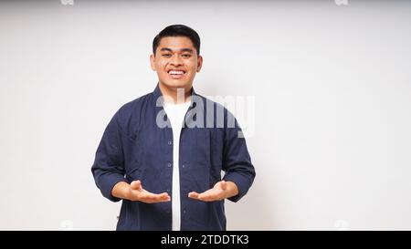 Junger asiatischer Mann lächelt mit einer Hand, die etwas auf weißem Hintergrund hält Stockfoto