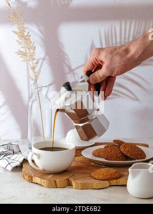 Die Hand eines Mannes gießt Kaffee in eine weiße Tasse Stockfoto