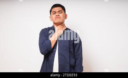 Junger asiatischer Mann, der seine Kehle berührt, mit Schmerzausdruck auf weißem Hintergrund. studio-Aufnahme Stockfoto