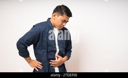 Junger asiatischer Mann mit schmerzhaften Magenschmerzen auf weißem Hintergrund Stockfoto