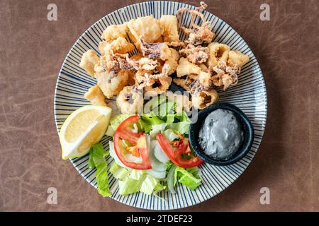 Ein Blick über einen Teller mit frisch gebratenen Calamare Tintenfischringen serviert Wing Tintenfischtinte Knoblauch Dip. Stockfoto