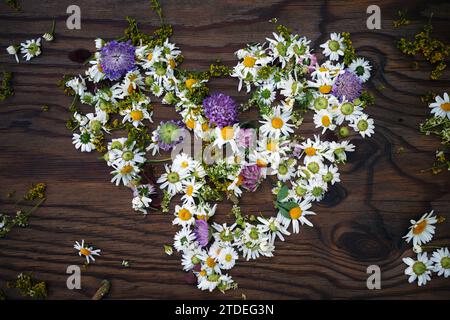 Herzsymbol aus Blumen auf Vintage-Holzhintergrund. Flache Lagen. Stockfoto