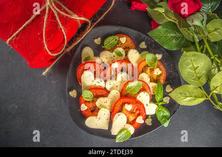 Caprese Salat zum Valentinstag Abendessen, mit Tomaten, Käse in Form von Herzen, Basilikum. Valentine day Menü Konzept Draufsicht Kopieplatz Stockfoto