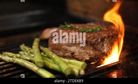 Kochen eines Rib-Eye-Steaks auf einem Grill, Grill oder grill. Ein großes Rippauge mit Knochen, das von einem Grill mit Flamme oder Aufflammung wegfliesst. Rindfleischkonzept Stockfoto