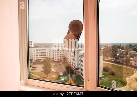 Ein moderner Staubsauger-Fensterreiniger reinigt Glas von Schmutz und Flecken auf einem pvc-Balkonrahmen. Sturzsicherheit. Stockfoto