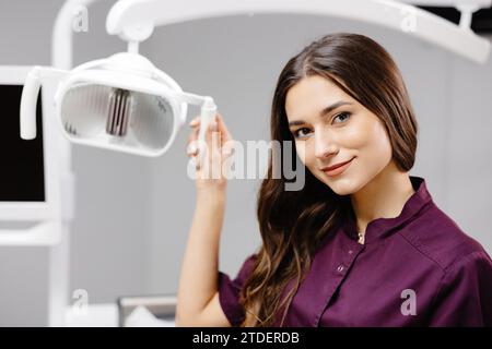 Kaukasische Zahnärztin, die vor der Behandlung die Lampe anschaltet, den männlichen Patienten lächelt. Stockfoto