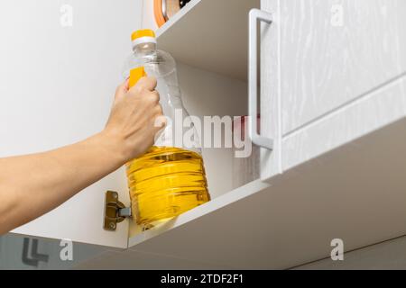 Die Hausfrau nimmt eine Flasche Sonnenblumenöl aus dem Küchenschrank. Frau, die eine Flasche Sonnenblumenöl hält. Stockfoto