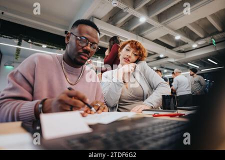 Geschäftsfrau, die ihren männlichen Kollegen beim Telefonieren beaufsichtigt. Sie hilft ihm, wann immer er es braucht. Stockfoto