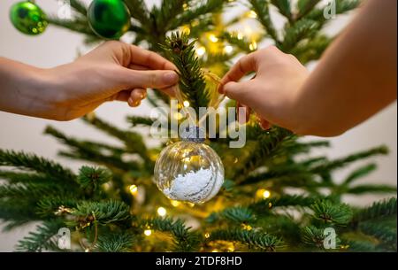 Eine Frau hängt einen Ball an einem Neujahrsbaum. Stockfoto