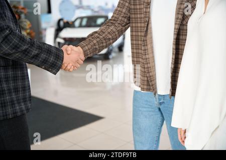 Mann schüttelt Hand mit Verkäufer, nachdem er ein Auto im Händlerzentrum gekauft hat Stockfoto