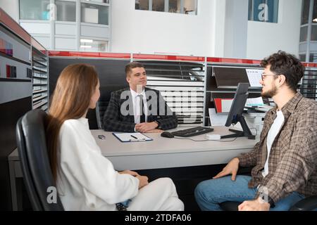 Ein Paar unterschreibt Dokumente über den Autokauf am Tisch mit einem Verkäufer Stockfoto