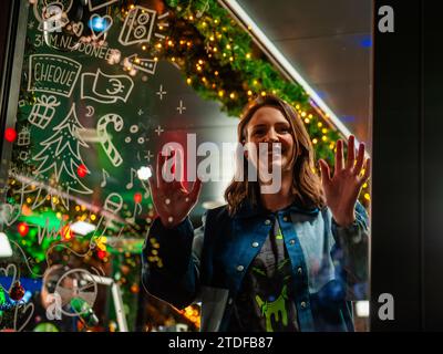 3FM DJ Sophie Hijlkema schaut durch das Fenster, nachdem er im Glashaus eingesperrt wurde. Am Grote Markt in Nijmegen hat gerade die Spendenaktion „3FM Serious Request“ begonnen. Jedes Jahr um diesen Tag herum werden 3FM-DJs (niederländischer Radiosender, der vom öffentlich-rechtlichen Sender NPO kontrolliert wird) bis Heiligabend in einem Glashaus eingesperrt. Von diesem Haus aus werden die DJs senden, um Geld für einen bestimmten Zweck zu sammeln. Dieses Jahr wird das Geld für die als-Stiftung (Amyotrophe Lateralsklerose) verwendet. Die DJs spielen Tag- und Nachtlieder, die die Hörer anfordern, gegen eine Spende. Stockfoto