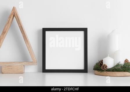 Schwarzes quadratisches Rahmenmodell mit einem Holzbaum und Kerzen auf einem weißen Tisch. Weihnachtsdekoration. Stockfoto