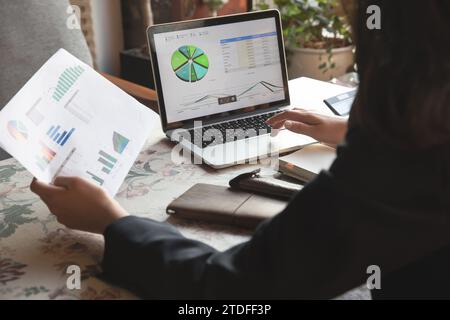 Frau, die Finanzanalysen mit einem Laptop am Fenster eines Cafés mit starkem Sonnenlicht macht Stockfoto