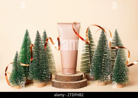 Beige Tube Kosmetikcreme, die auf dem Wald in der Nähe vieler Weihnachtsbäume liegt. Winter Bio Kosmetik. Behandlung Spa Schönheit Hautpflege Stockfoto