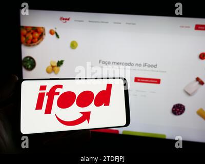 Person mit Smartphone und Logo der brasilianischen Lebensmittelbestellungs- und Lieferfirma iFood vor der Website. Schwerpunkt auf dem Display des Telefons. Stockfoto